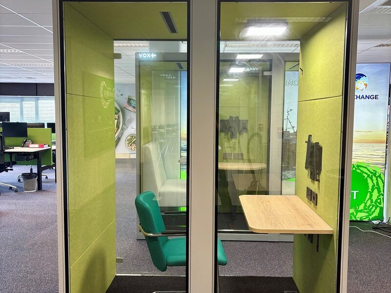 VOX Medium met groene stoffering en zwart frame als focusplek in de kantoortuin.